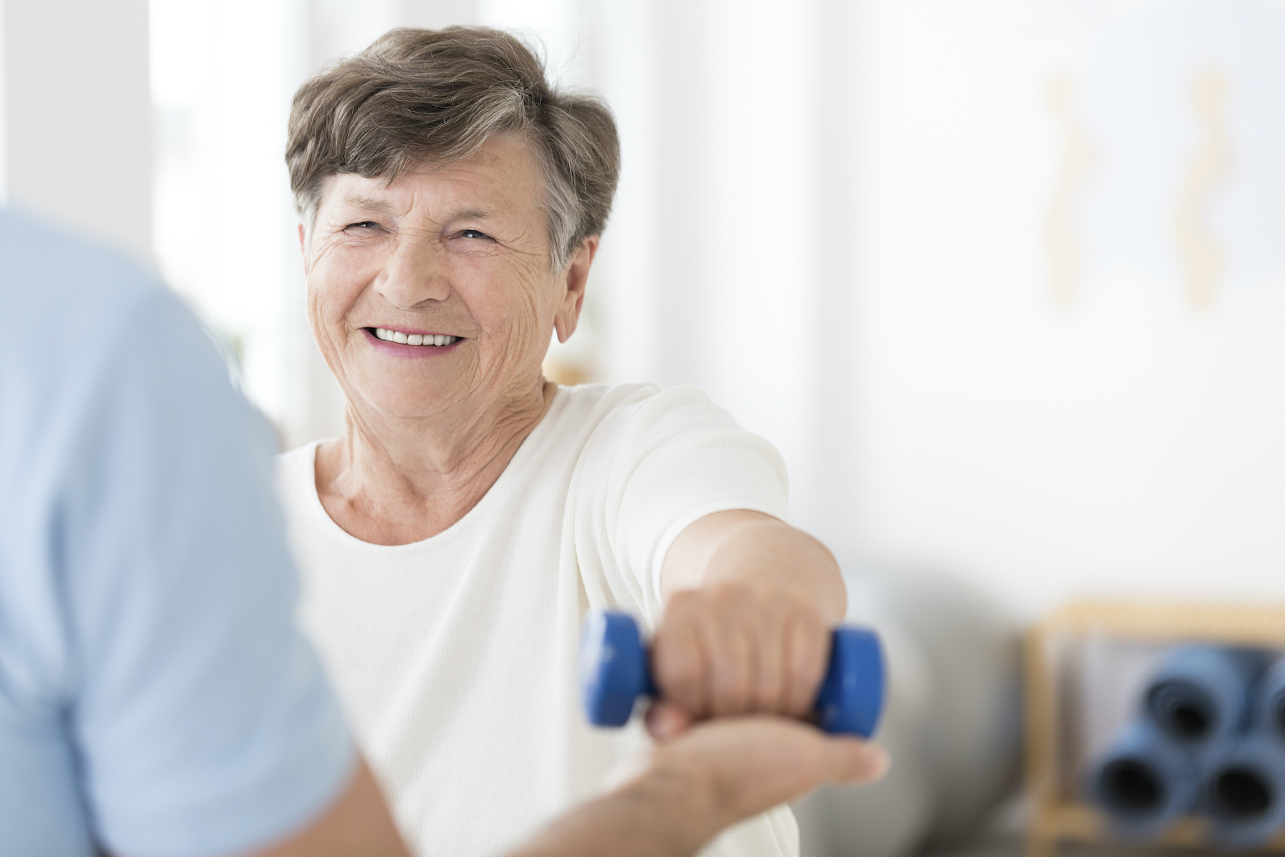 Happy senior woman exercising arms with small weights with help from a physiotherapist