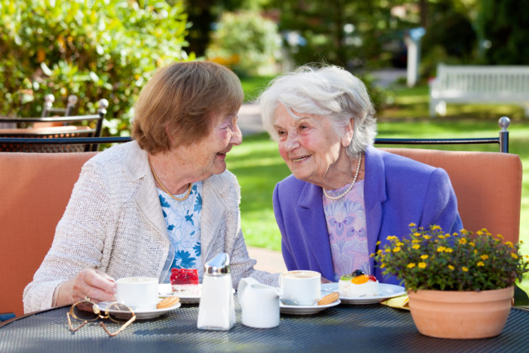 Dos mujeres mayores relajándose en una mesa al aire libre.