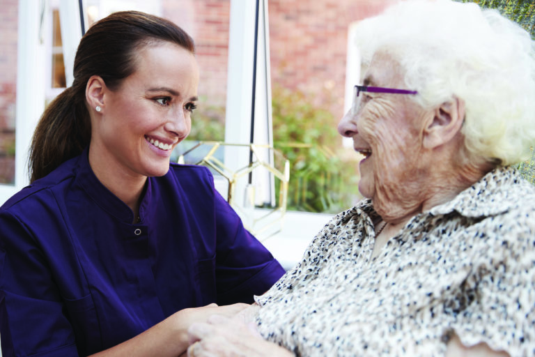 Mujer residente sentada en una silla y hablando con un cuidador en una residencia de ancianos