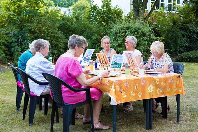 Group of senior women sitting at table and painting outdoors