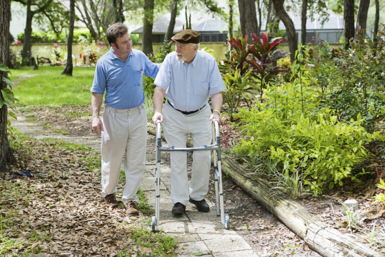 Young male and elderly man with walker walking outside