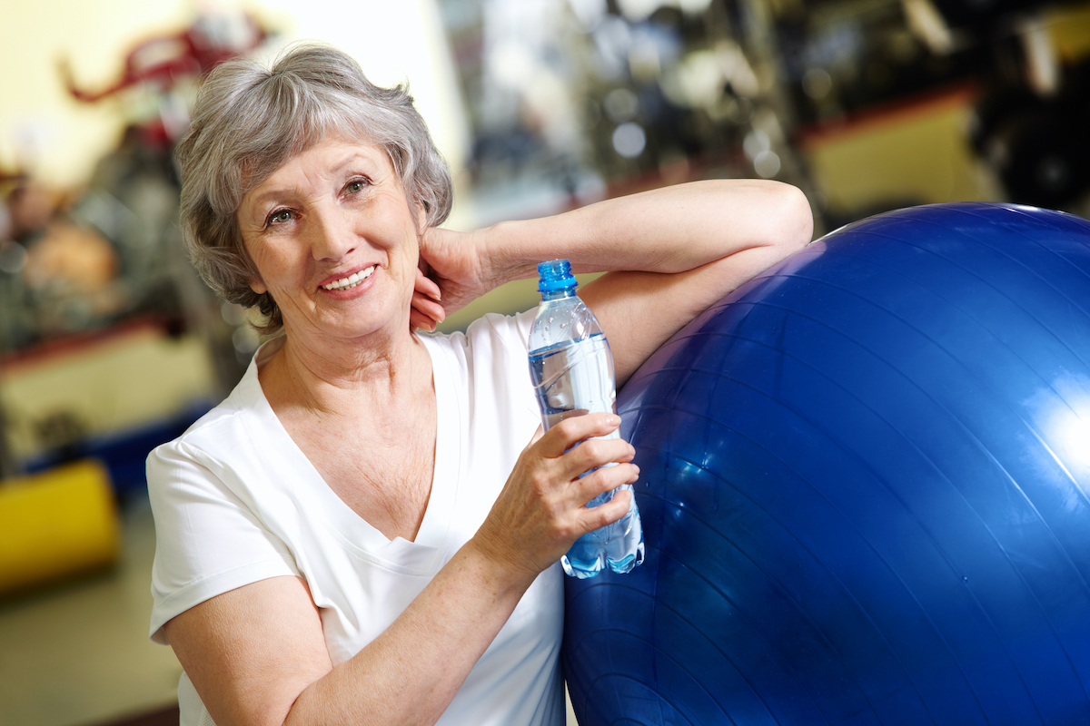 Senior woman with leaning on exercise ball land holding water bottle
