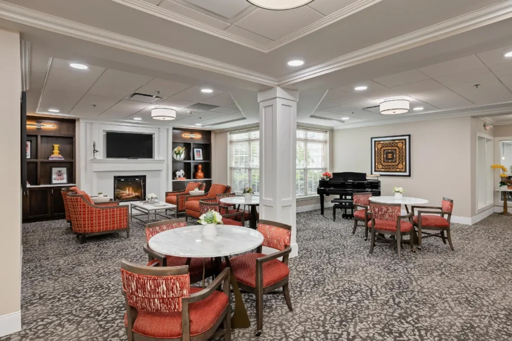 Assisted living gathering space with tables, chairs, piano and fireplace