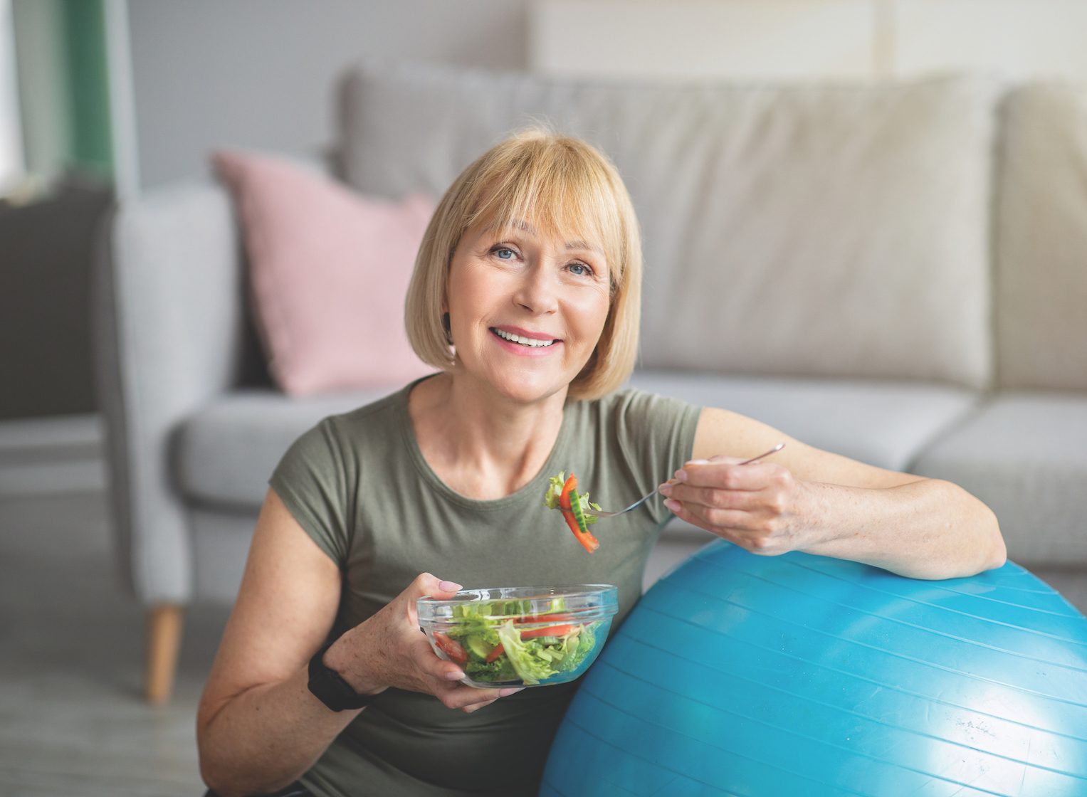 Senior woman leaning on exercise ball holding salad