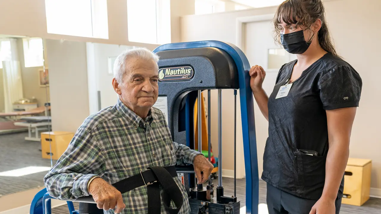 Metropolis therapist with senior male resident on exercise machine