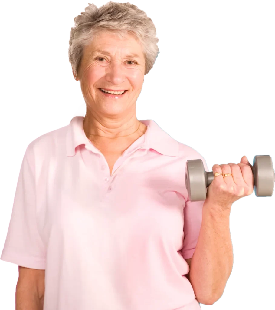 An elderly woman with short gray hair, wearing a light pink polo shirt, is smiling while holding a gray dumbbell in her right hand, positioned near her shoulder. She is engaged in a light workout activity.