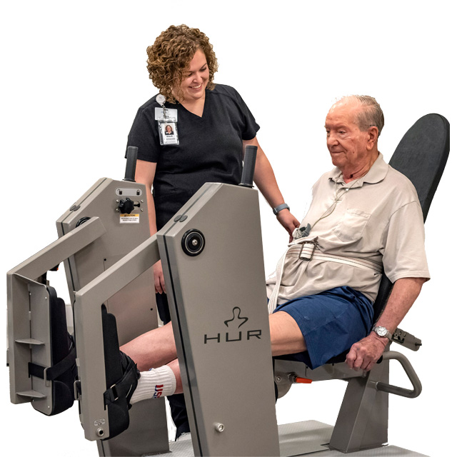 Therapist helping senior male resident use a leg weight machine