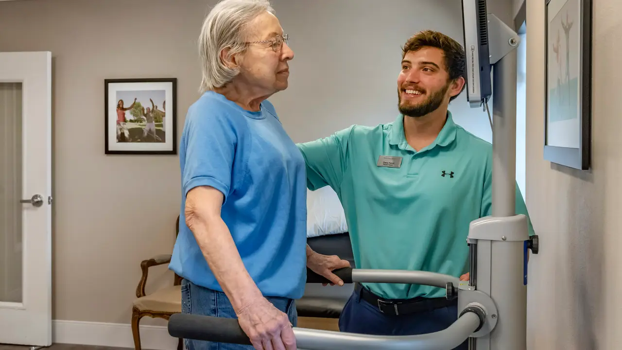 Therapist helping senior female resident walk on machine
