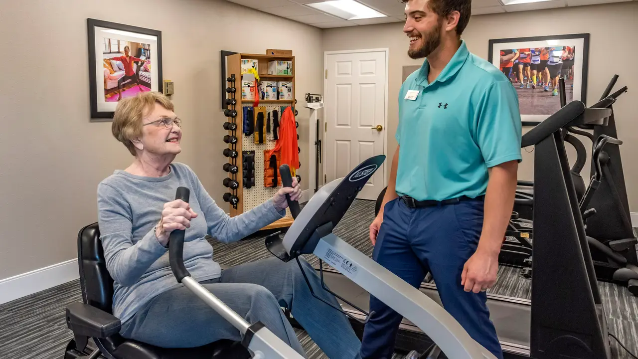 Therapist helping senior female resident pedal on indoor cycle machine