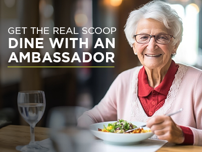 An elderly woman with short white hair and glasses smiles while dining in a restaurant. She wears a red blouse under a pink cardigan. The text overlay reads, 