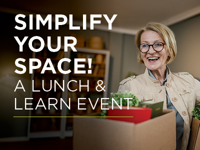 A smiling woman with glasses holds a box filled with household items. The text reads, “Simplify Your Space! A Lunch & Learn Event by Assisted Living Muskogee.” The background features shelves and home decor.