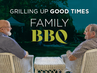Two older men sit facing each other across a white wicker table outdoors, smiling and relaxing at their assisted living community. Text reads: 