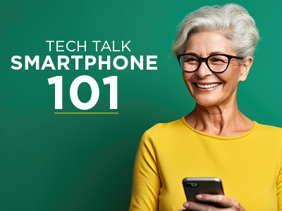 An elderly woman with short gray hair and glasses, smiling while holding a smartphone, stands against a green background. The text reads 