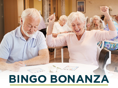 An elderly woman joyfully raises her arms in celebration while playing bingo at an assisted living center next to an elderly man who is focused on his bingo card. The background features other seniors engaged in the game. The text 