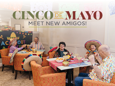 Four seniors in sombreros enjoy food and drinks at a festive Cinco de Mayo celebration in an Assisted Living community. Colorful banners brighten the room. Text reads: