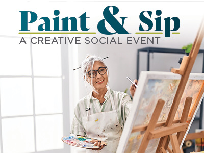 Smiling woman with gray hair and glasses paints on a canvas at an easel in a bright Senior Living space, holding a palette and brush. Text above her reads, “Paint & Sip: A Creative Social Event.” Sunlight streams in through a window behind her.