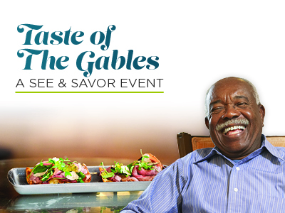 Smiling man in a blue shirt sits beside a plate of gourmet sandwiches at an Assisted Living event. Text reads
