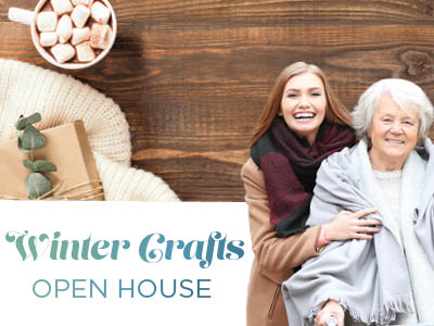 A young woman and an older woman smile together, wrapped in cozy winter clothing. Nearby are a mug of hot chocolate with marshmallows, a wrapped gift, and eucalyptus leaves. Text reads: