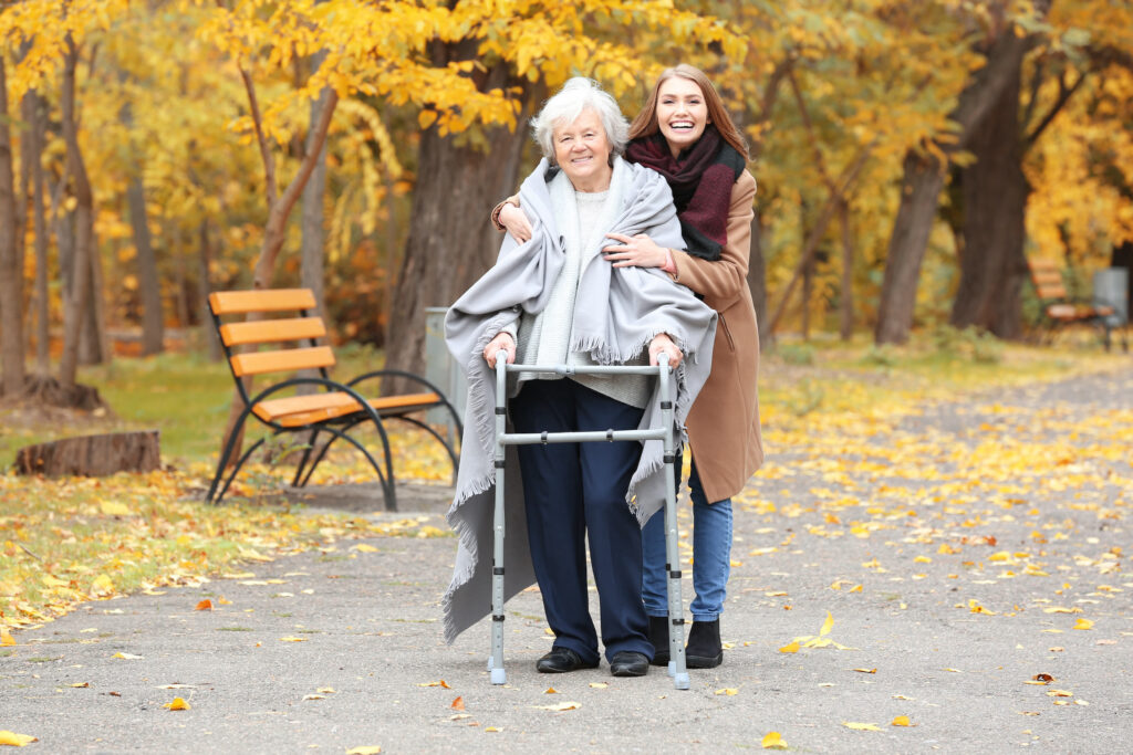 Daughter walking with senior mother using walker in park 