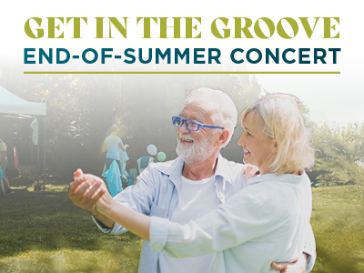 Smiling older couple dancing outdoors on grass under a sunny sky at a Senior Living Community event, with people and a tent in the background. Text above them reads 