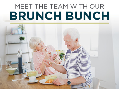 Two smiling older adults sit at a kitchen table enjoying brunch together. The text above them reads, 