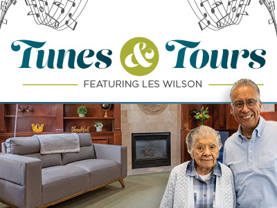 Two smiling seniors stand in front of a cozy Assisted Living & Memory Care living room with a fireplace and sofa. Above them, text reads