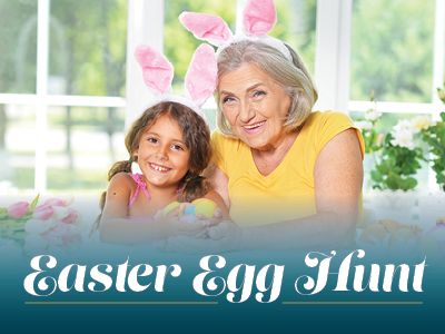 Smiling elderly woman and young girl wearing bunny ears sit together at a table with Easter eggs. The text