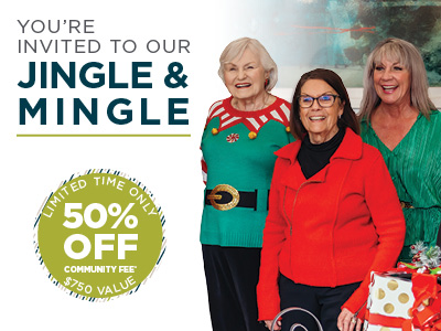 Three smiling older women stand together, one wearing a festive sweater, next to a sign that reads 