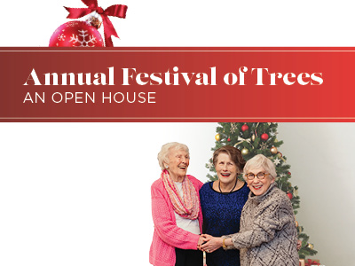 Three elderly women stand and smile in front of a decorated Christmas tree at Charlestown Senior Living Community. Above them, a red banner with a holiday ornament reads