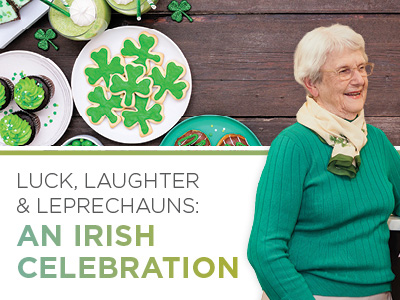 An elderly woman in a green sweater smiles beside a table with shamrock-shaped cookies, cupcakes, and green treats. Text reads: