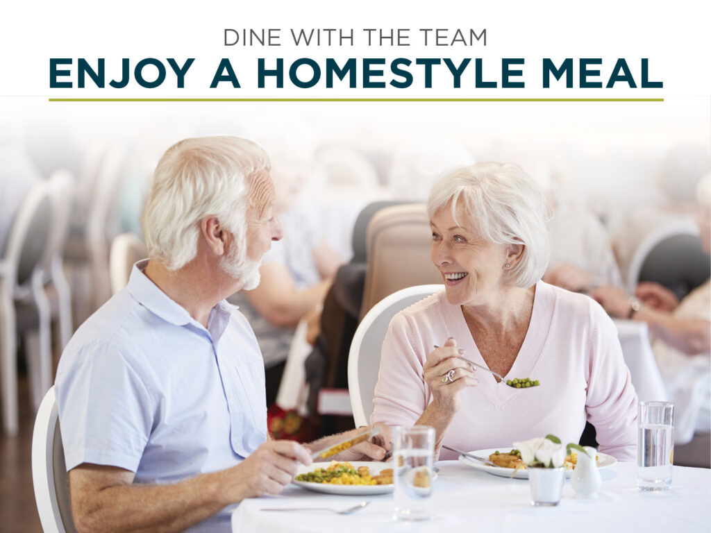 An elderly man and woman smile and chat while dining together at a restaurant. The table is set with plates of food, glasses of water, and napkins. The background shows several other diners. The text at the top reads, 