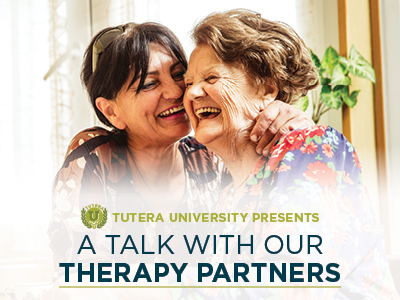 Two smiling elderly women share a warm embrace in a bright room with green plants. The text reads, 