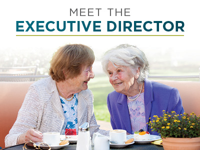 Two elderly women sit at a table outdoors, smiling and talking over coffee and dessert. Text above them reads, 