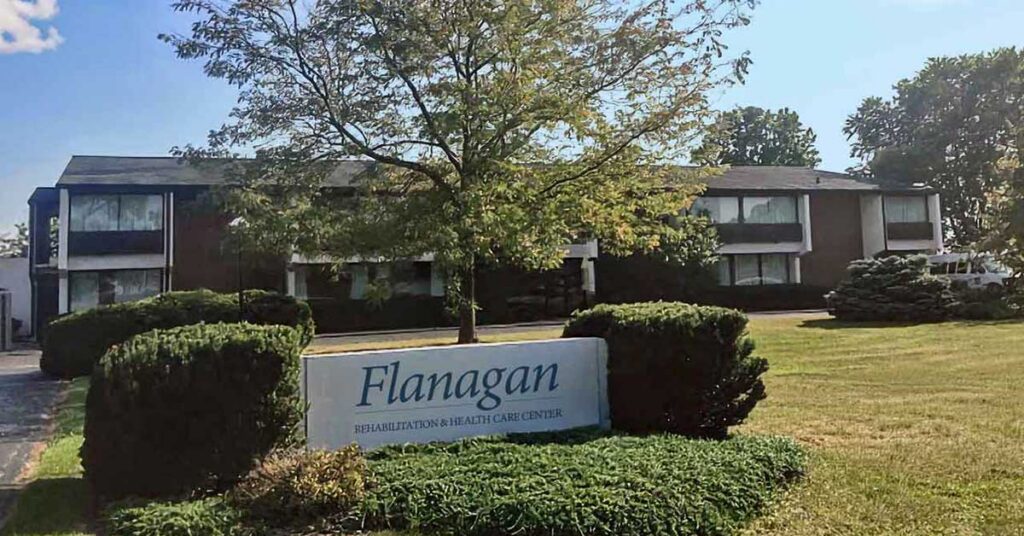 A two-story building with large windows, surrounded by trees and bushes. In front, a sign reads 