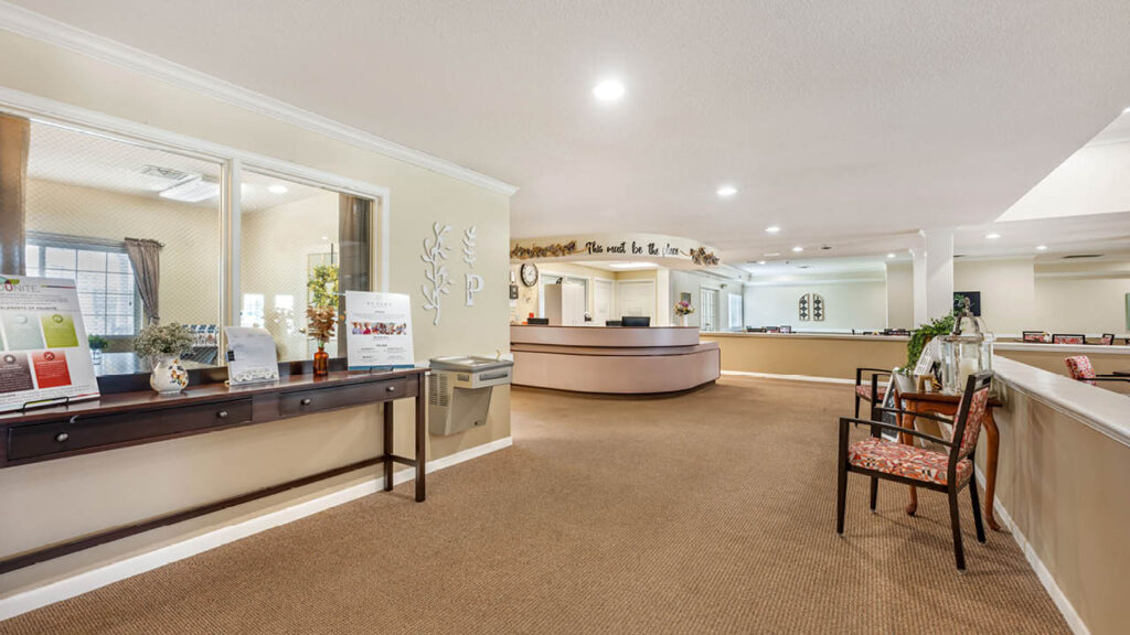A spacious, well-lit reception area with a large curved front desk, chairs with patterned cushions, brochures on a side table, and neutral-colored walls and carpeting.