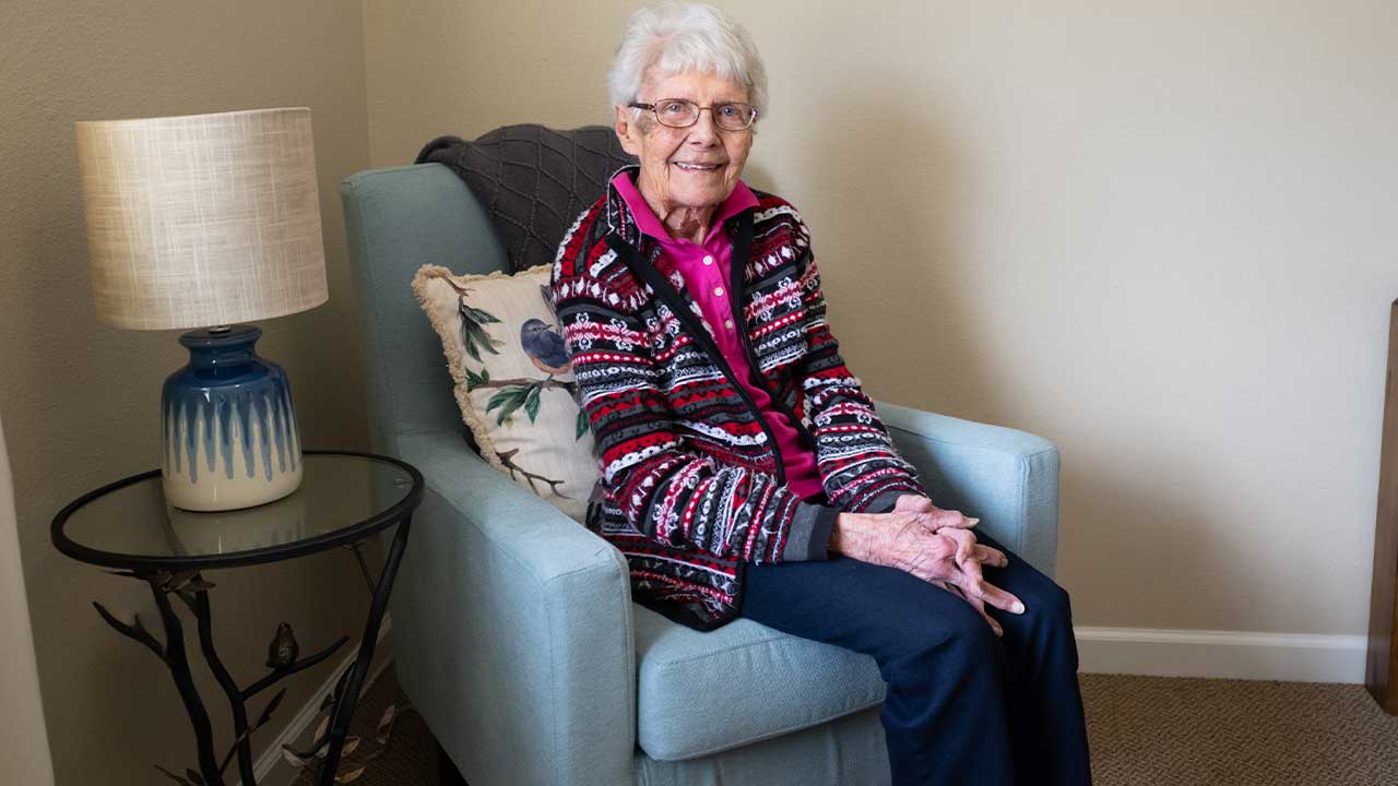 Female senior resident smiling sitting in blue chair at Pathfinder Senior Living