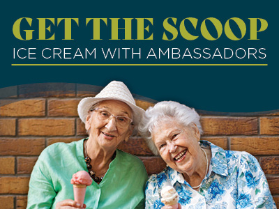Two smiling elderly women sit together enjoying ice cream cones at a Senior Living Community event. One wears a white hat and green shirt, the other a blue floral shirt. The text above reads,