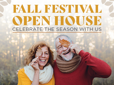 Smiling older couple holds autumn leaves over one eye, dressed in cozy sweaters and scarves, standing outdoors with fall trees. Text reads: “Fall Festival Open House. Celebrate the season with us.”.