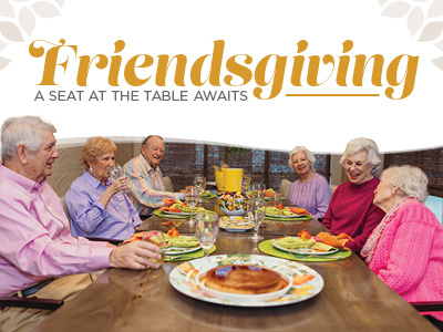 A group of six seniors smiling and talking around a dinner table set for Friendsgiving.