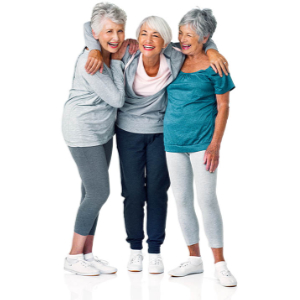 Three elderly women, smiling and standing close together in the community room of their 55+ apartments, wear casual gray and teal clothing with white sneakers. They have short gray hair and show camaraderie with their arms around each other, set against a plain white background.