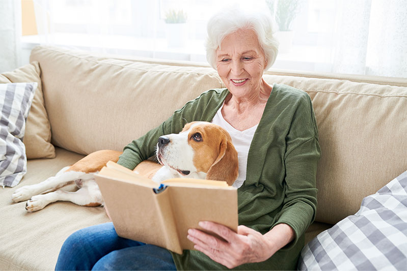 Senior woman reading on the couch while dog lies in her lap