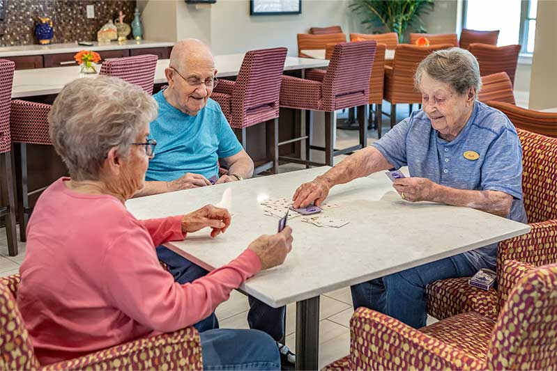 Two senior women and one senior man playing cards at dining table