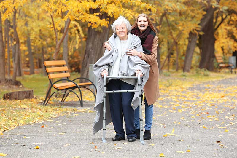 Woman and senior with walker walking on outdoor path in the fall