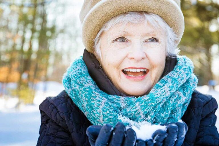 Senior woman holding snow outside in the park