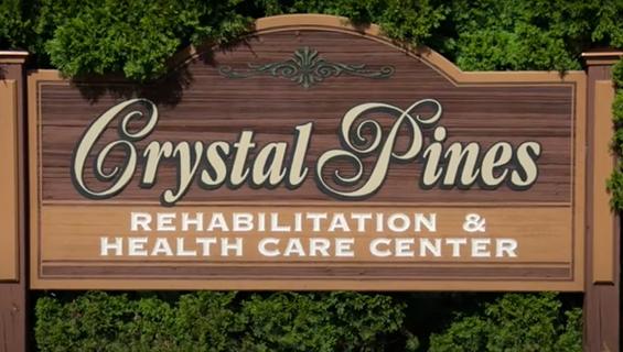 Sign for Crystal Pines Rehabilitation & Health Care Center, featuring a wood texture background with green foliage on the sides.