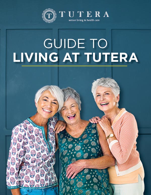 Three smiling older women stand together against a dark teal background. They are dressed in colorful, casual clothing. The text above them reads "Guide to Living at Tutera.