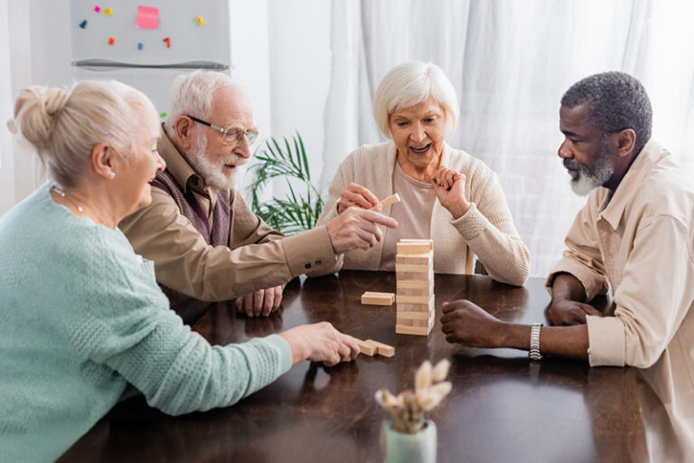 Four older adults are gathered around a wooden table, playing a game of Jenga