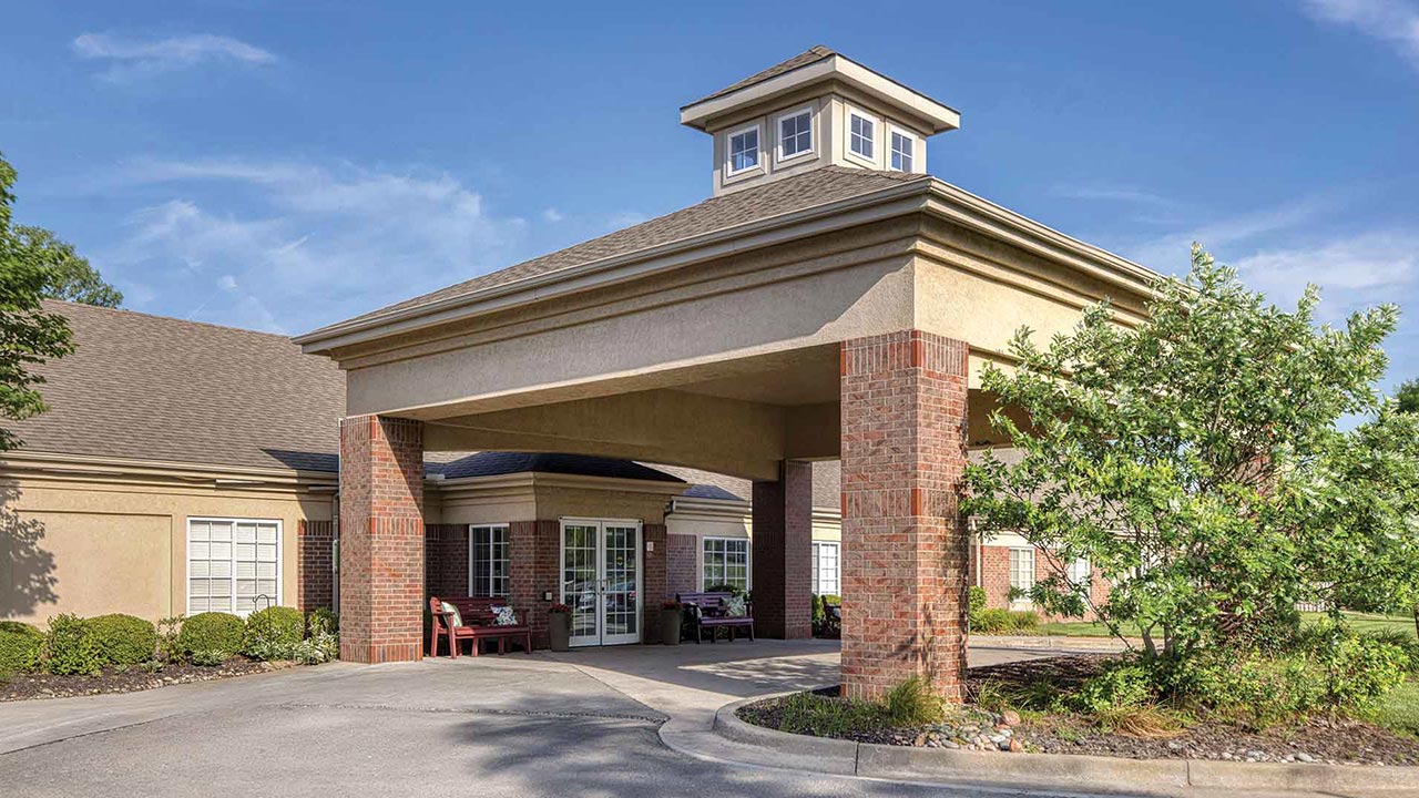 Exterior of a single-story building featuring a large covered entrance with brick pillars and a cupola on the roof.