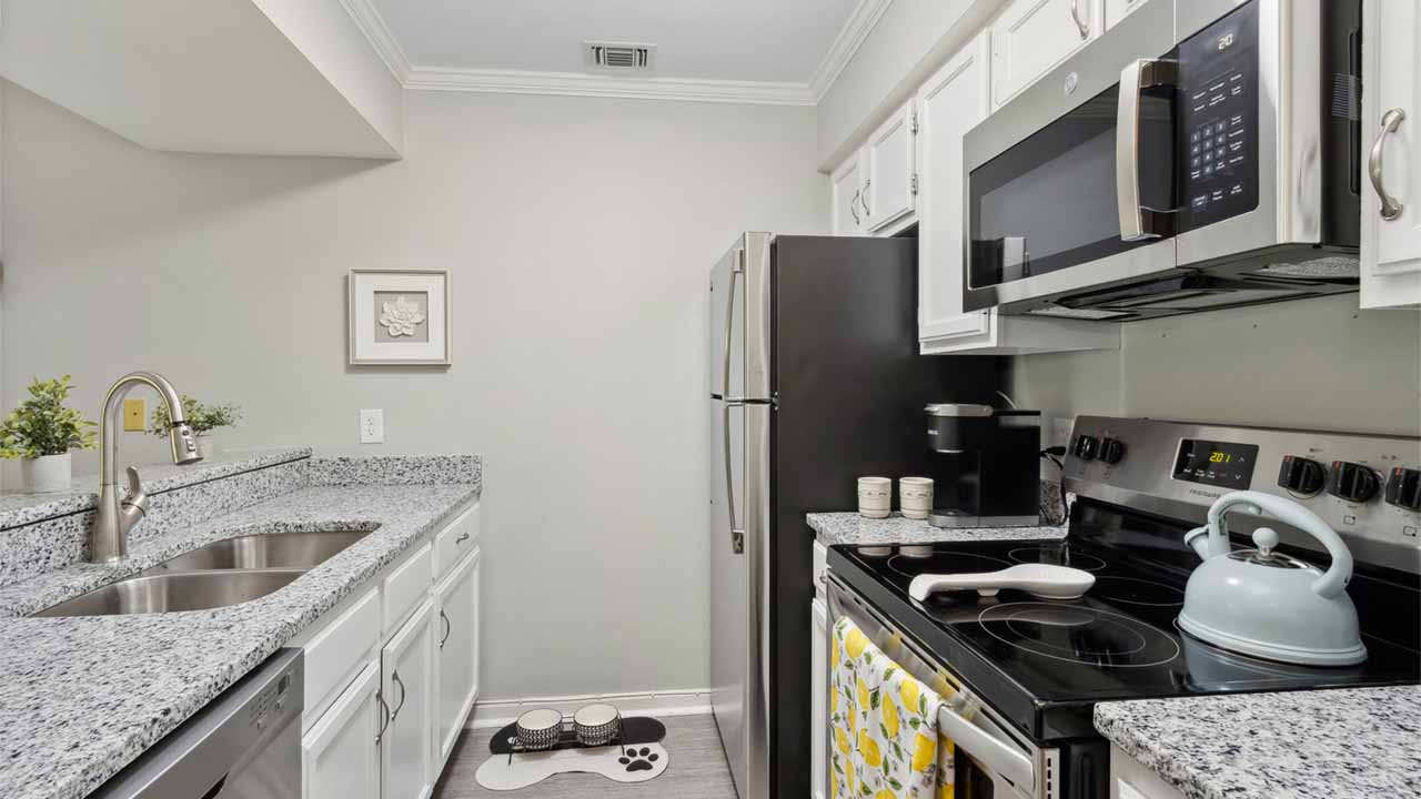 Modern kitchen with white cabinets, granite countertops, stainless steel appliances, a stove with a blue kettle, sink with double basins, and a pet feeding area on the floor with bowls and a paw print mat.