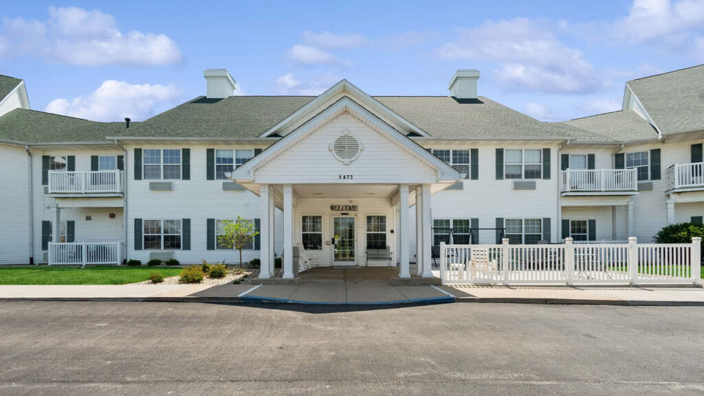 A two-story white building with green roofing, front porch, and columns. A 